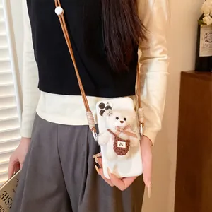 Detail of white phone case featuring a plush bear charm and brown woven crossbody strap