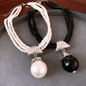 Détail d'élégants colliers de perles multi-rangs noirs et blancs avec gros pendentifs.