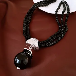 Gros plan d'un collier de perles noires à plusieurs rangs avec un pendentif imposant