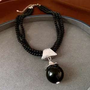 Gros plan d'un collier de perles noires à plusieurs rangs avec un grand pendentif sphérique.