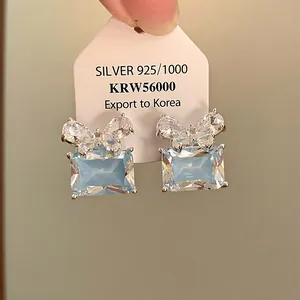 Gros plan sur des boucles d'oreilles rectangulaires bleu clair avec nœud en zircon