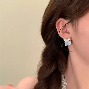 Gros plan d'une boucle d'oreille carrée en zircon avec un nœud élégant sur l'oreille