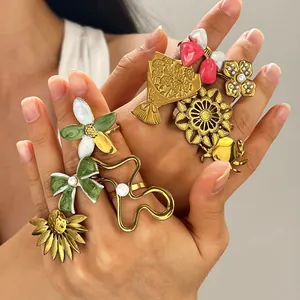 Collection of vintage colorful enamel rings featuring floral and bow designs on hands.