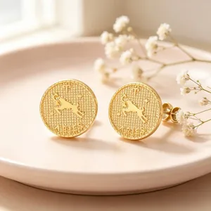 Gold Aries constellation relief coin stud earrings in stainless steel on a soft pink plate.