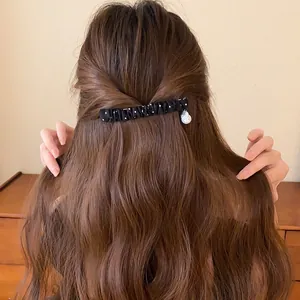 Detailopname van een elegante zwart-witte haarclip van geplooide stof met stippen in bruin haar.