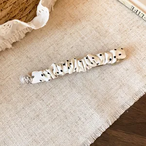 Detail van een witte geplooide stoffen haarspeld met zwarte stippen op een linnen achtergrond.