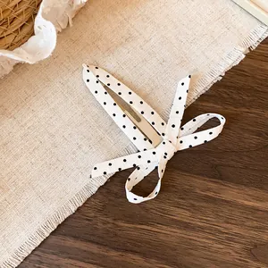 Detailweergave van een haarclip met een zwart-witte polkadotstrik op linnen tafel