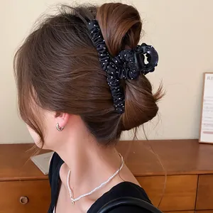 Detail van een elegante zwart-witte haarclip van geplooide stof met stippen gedragen door model