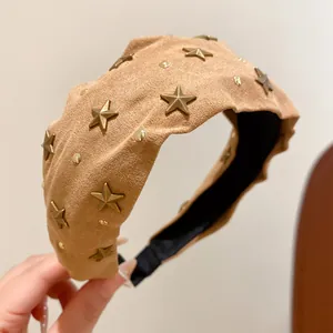 Close-up detail of a beige suede headband featuring vintage gold star and stud accents