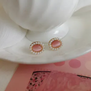 Close-up of vintage-style oval pink cat eye earrings with pearl border on white porcelain