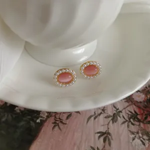 Close-up detail of vintage oval earrings featuring pink cat eye stones and pearl accents