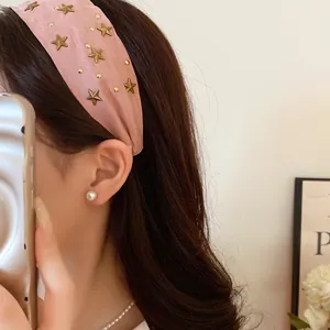 Detail view of a pink fabric headband decorated with gold star studs on a model.
