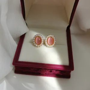Detailed view of vintage oval pink cat-eye earrings with pearl halo inside a red jewelry box