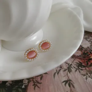 Macro detail of retro oval earrings with pink cat-eye stone and small pearl border