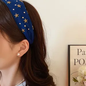 Detail view of a navy blue fabric headband featuring gold star studs on a model