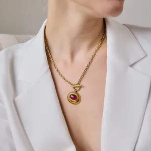 Nahaufnahme einer goldenen Titanstahlkette mit rotem Harzanhänger und OT-Verschluss.