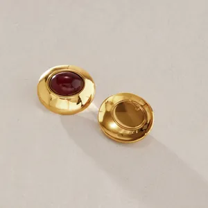 Nahaufnahme von goldenen Ohrsteckern mit dunkelrotem Harz-Cabochon und Metallrückseite.
