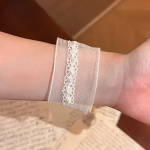 Detailansicht eines weißen Schneegaze-Armbands mit Perlen und Spitzenverzierung.