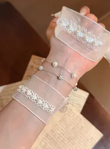 Detailaufnahme eines weißen Organza-Armbands und feiner Perlenkette am Handgelenk