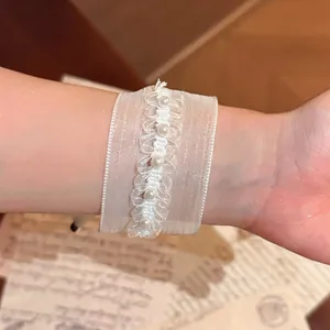 Detailansicht eines weißen Organza-Armbands mit Perlenperlen an einem Handgelenk