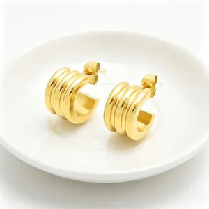 Close-up of golden stainless steel triple-layered C-shaped hoop earrings on white dish