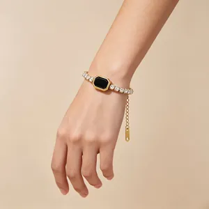 Elegante bracciale tennis dorato con gemma nera quadrata sul polso di una modella