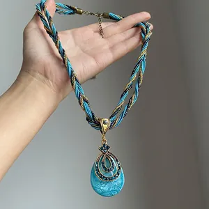 Vue détaillée d'un collier bohème avec pendentif goutte et strass, tenu à la main pour la taille.