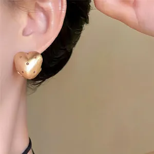 Primo piano di un orecchino a cuore dorato opaco a pois indossato sull'orecchio