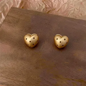 Vista dettagliata di orecchini a cuore in oro opaco con eleganti pois neri