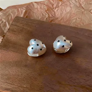 Dettaglio di orecchini a cuore in argento opaco con motivo a pois neri a olio