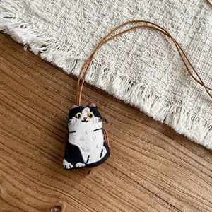 Handmade embroidered fabric cat pendant necklace with brown leather rope on wooden background