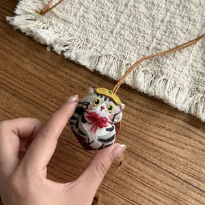 Detailed view of a cute embroidered cat doll pendant attached to a brown leather cord.