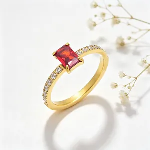 Close-up van gouden stalen ring met rechthoekige rode zirkoon en halve diamantband