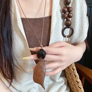 Close-up van een boheemse ketting met houten en stenen hanger op model gedragen.
