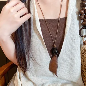 Gedetailleerde close-up van een vintage bohemian leren ketting met houten blad hanger.