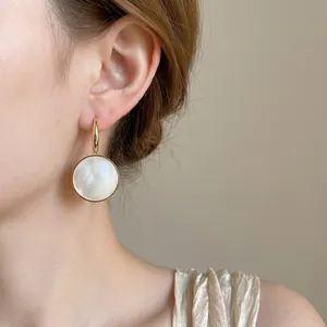 Eleganti orecchini a gancio dorati con un ciondolo circolare minimalista in conchiglia