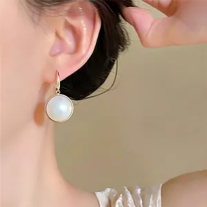 Primo piano di orecchini d'oro eleganti con pendente rotondo in conchiglia bianca