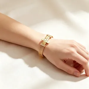 Gold stainless steel mesh bracelet featuring a Greek key cross charm on a woman's wrist