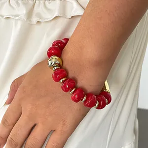 Detailansicht eines roten Acryl-Perlenarmbands mit goldenen Zwischenstücken am Handgelenk.