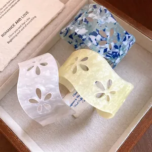 Three hollow floral acrylic open cuffs in marble blue, white, and yellow colors.