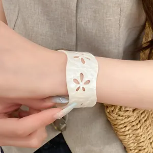 Close-up of minimalist white acrylic bangle with hollowed-out floral pattern details.