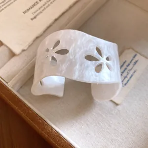 Close-up of minimalist white acrylic cuff bracelet with cutout flower patterns.