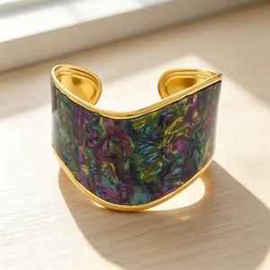 Macro detail of a V-shaped gold-plated cuff bracelet with colorful marble resin inlay.