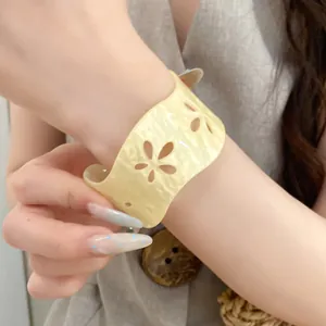 Close-up of a light yellow acrylic cuff bracelet with elegant hollow floral cutouts