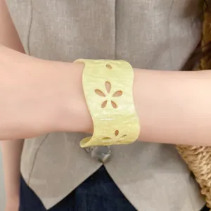 Detailed close-up view of a pale yellow acrylic open cuff bangle with hollow flower pattern