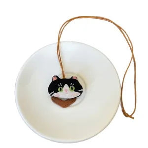Handgemaakte schattige ketting met geborduurde stoffen kat en bruin leren koord op bord