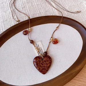 Detail of a bohemian leopard print heart necklace with amber beads on brown cord.