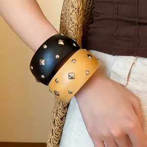 Detalle de brazaletes anchos retro con tachuelas metálicas plateadas redondas y rombos