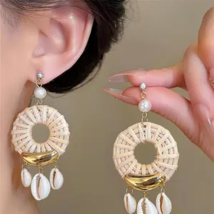 Detailed macro view of Bohemian straw woven earrings with dangling shell charms and pearls