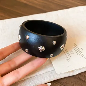 Vista detallada de un brazalete negro ancho con tachuelas plateadas redondas y de rombo